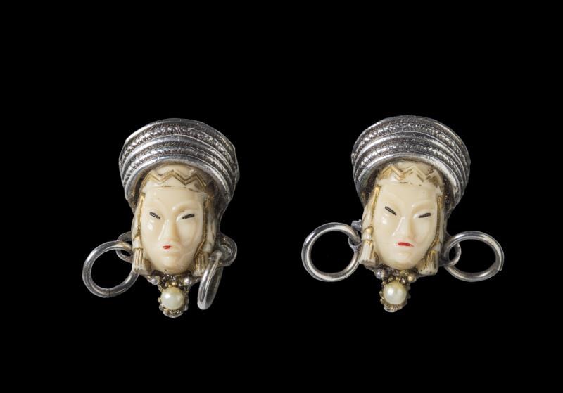 Coppia di bottoni con volti femminili dai tratti orientaleggianti in resina, metallo argentato e perle artificiali, sec. XX (metà)